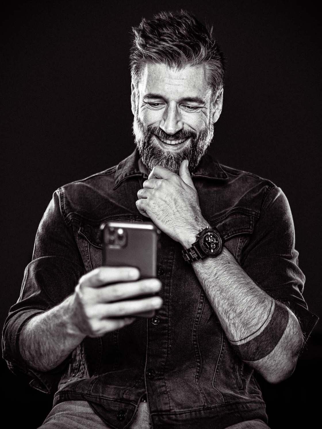 Portrait en noir et blanc d'Alexandre Comtois, souriant, cellulaire à la main