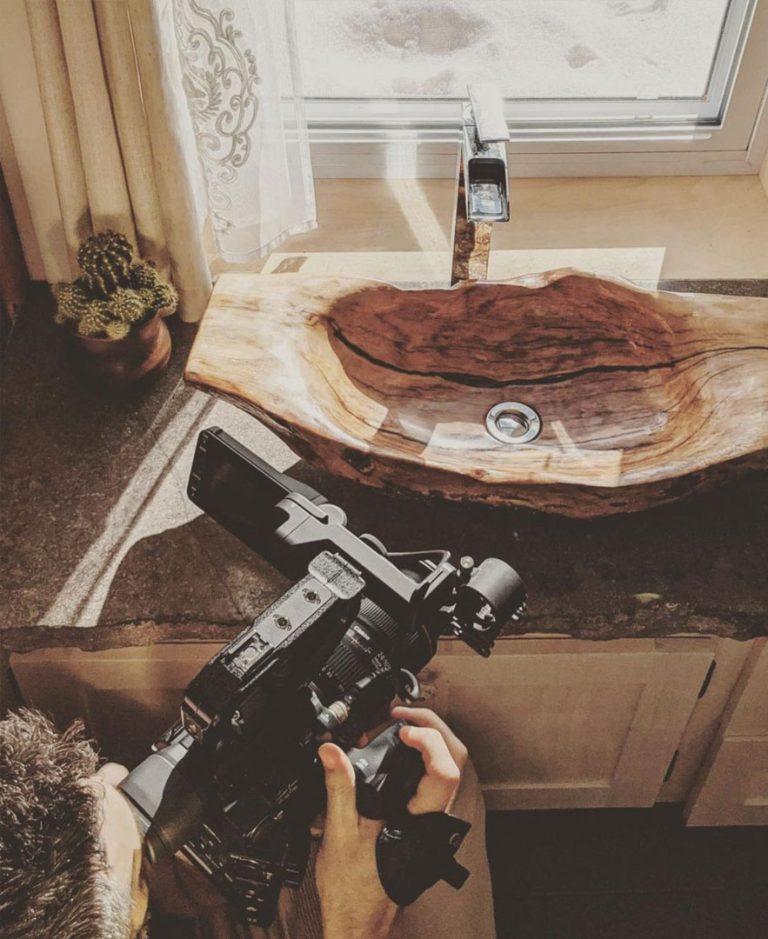 Les mains d'Alexandre Comtois sur sa caméra, filmant un lavabo taillé dans une bille de bois