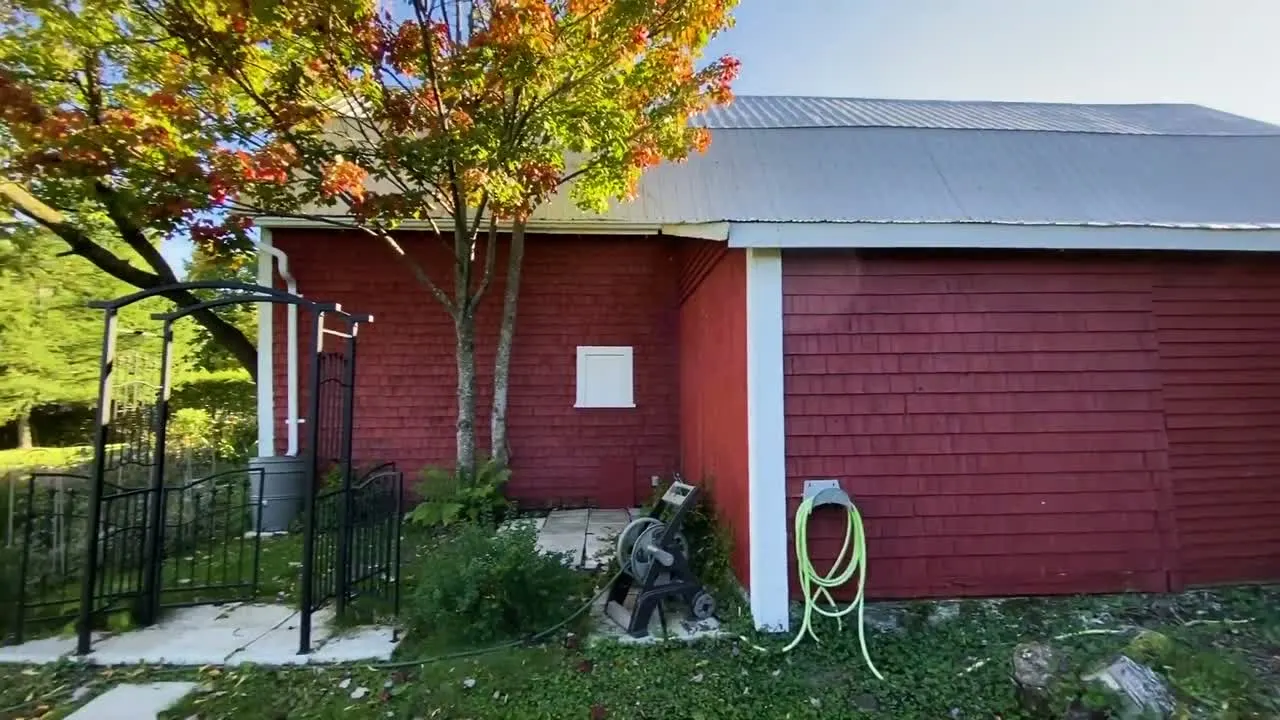 Une grange rouge au toit de tôle, sous un érable aux couleurs d'automne