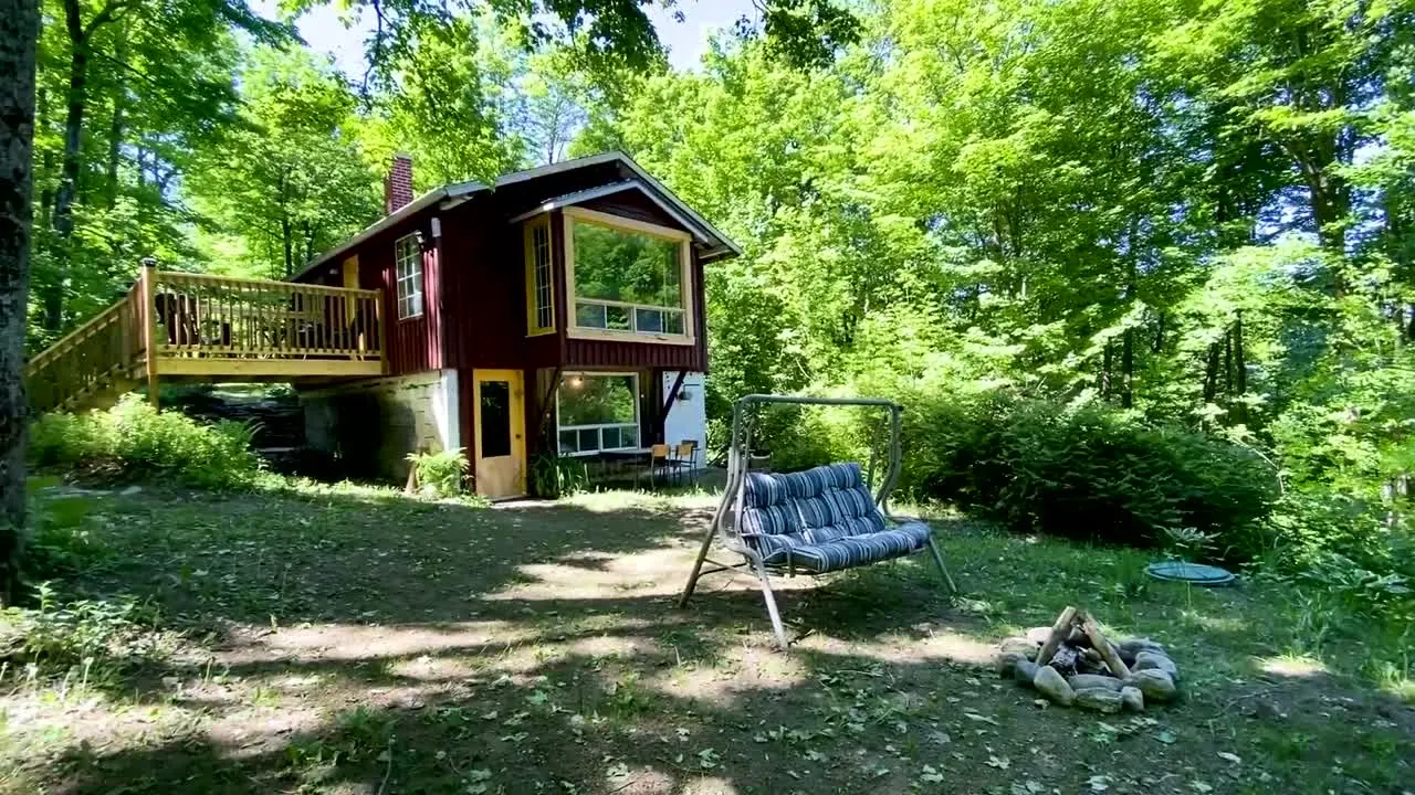 Une maison de bois rouge avec une grande galerie, au milieu des arbres