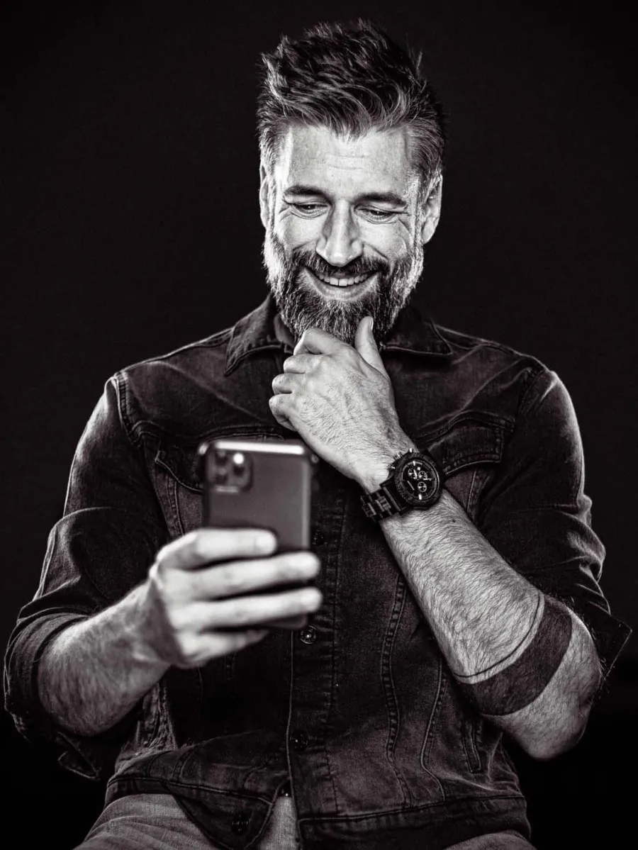 Portrait en noir et blanc d'Alexandre Comtois, souriant, cellulaire à la main